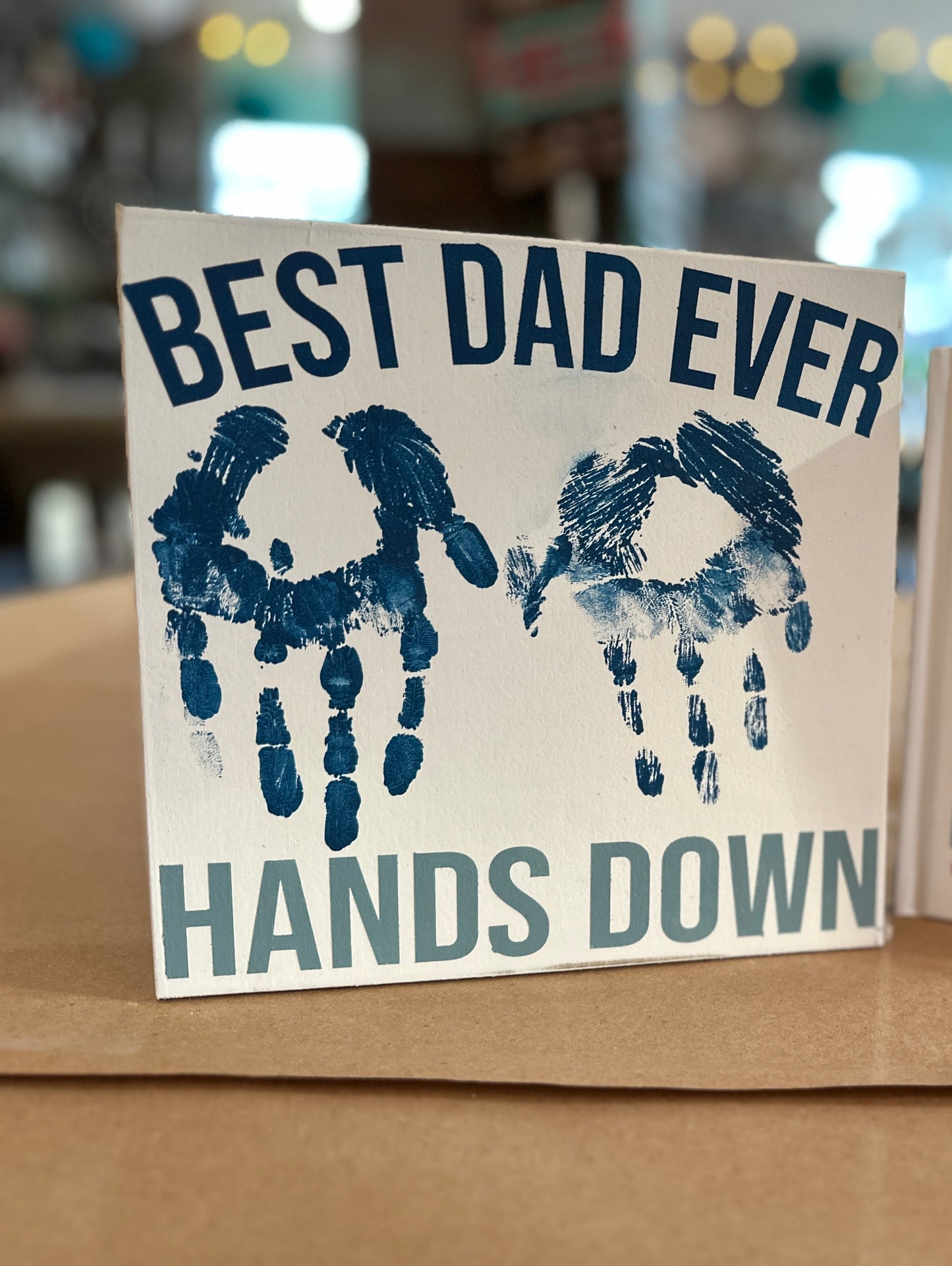 Create a custom sign for dad that says, "Best Dad Ever Hands Down" with your child's handprints in the center