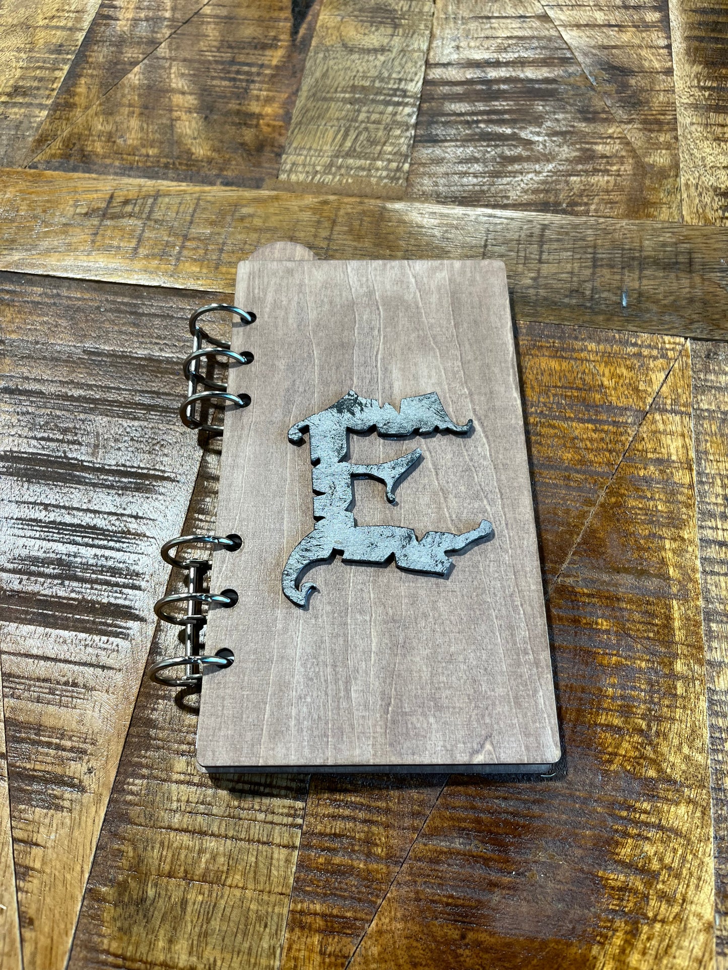 Notebook with laser-cut wood frame including letter E decoration. Metal spiral rings binding it.