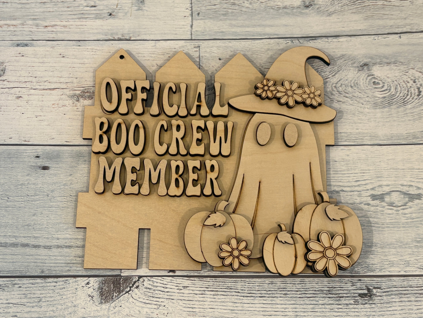 Laser cut sign of a fence with a ghost surrounded by pumpkins on it. Ghost has flowers on hat, farmhouse chic decor.