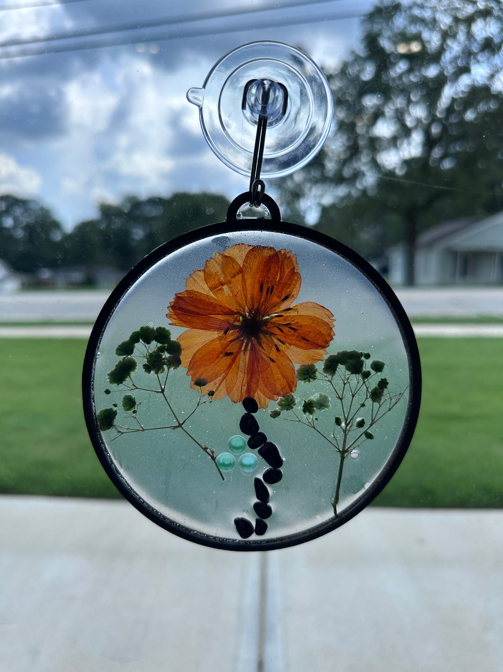 Circular window-hanging art with floral design and tumbled gemstone, arranged to look like w flower with a wavy stem.