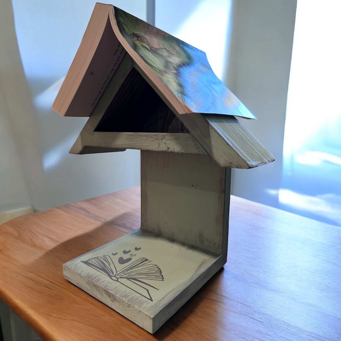 A wooden book rest with a shelf, featuring a roof shaped like the cover of a book, and storage.
