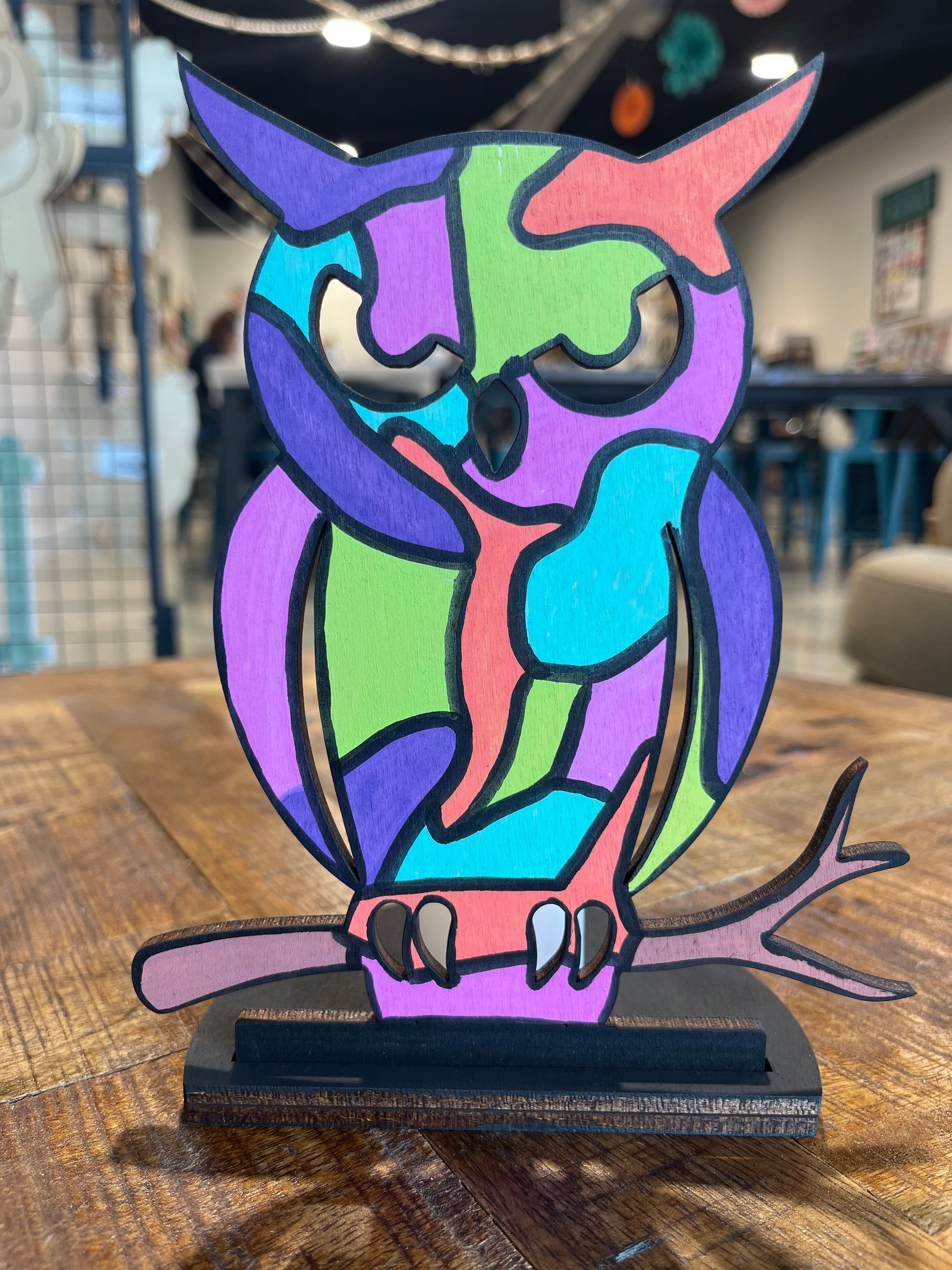 This votive includes a semi-circle, hand sized black base. The bas supports an owl, painted with bright abstract colors like lime-green and turquoise. The eyes, beak, and claws are cutouts so the candle behind the design can shine through.
