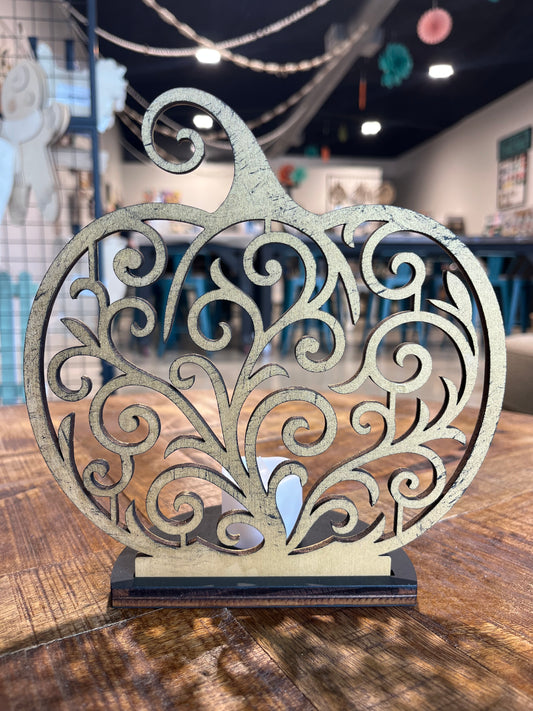 A hand sized, half-circle black base holds up a scroll design pumpkin with a tea candle behind it, creating a cozy glow.