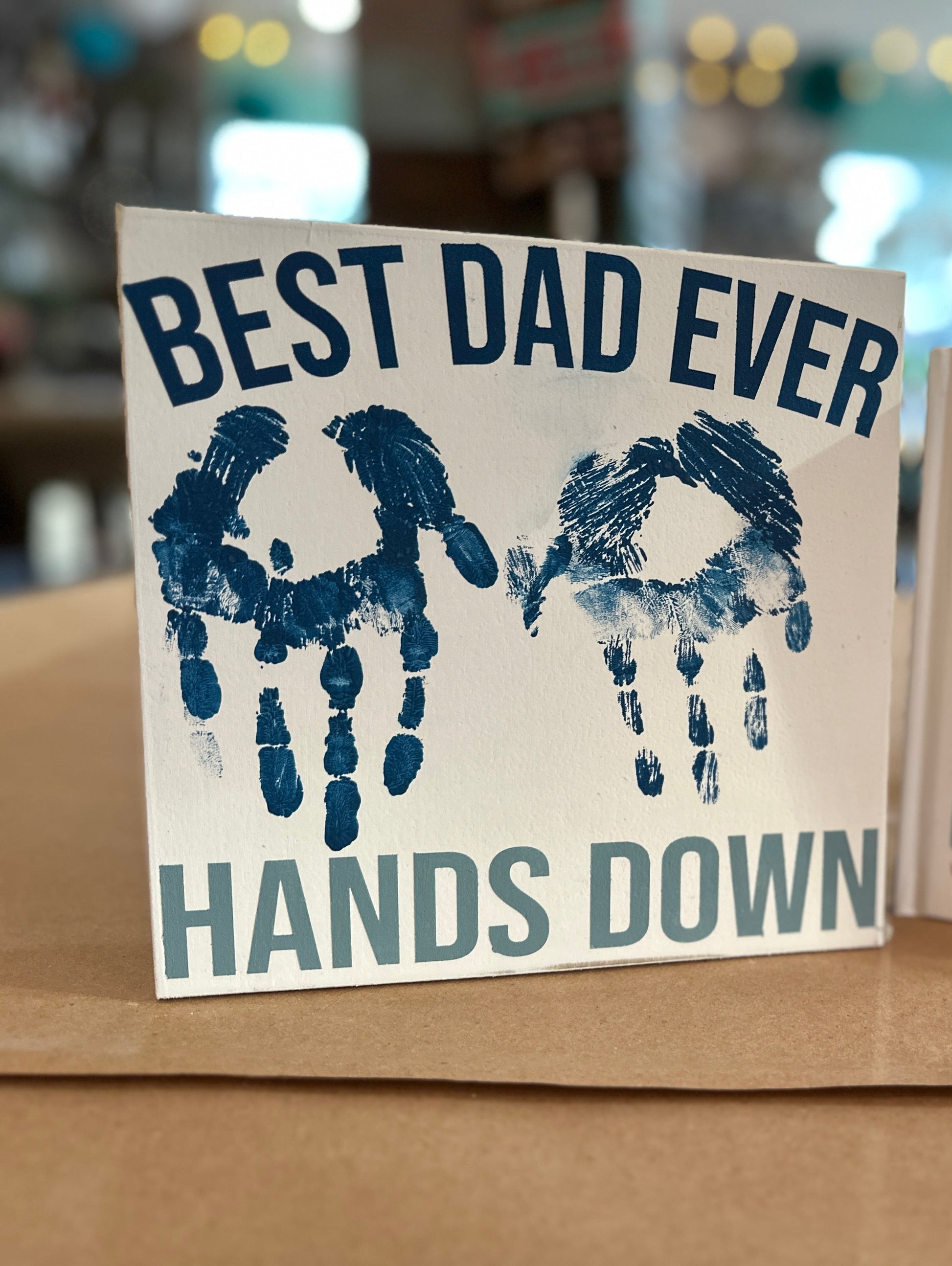 Create a custom sign for dad that says, "Best Dad Ever Hands Down" with your child's handprints in the center