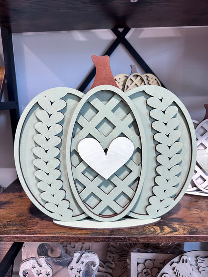 Decorative laser-cut pumpkin painted sage green with white heart and knit pattern.