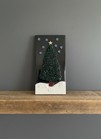 Decorative Christmas tree on a black background with snowflakes and a star, placed on a wooden surface against a gray wall.