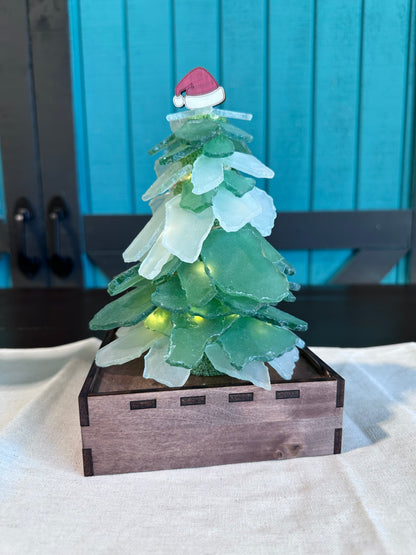 3-D sea glass tree on a wooden box base. The tree has a Santa hat topper, and lights wrapped around the inside to give it a cozy glow.