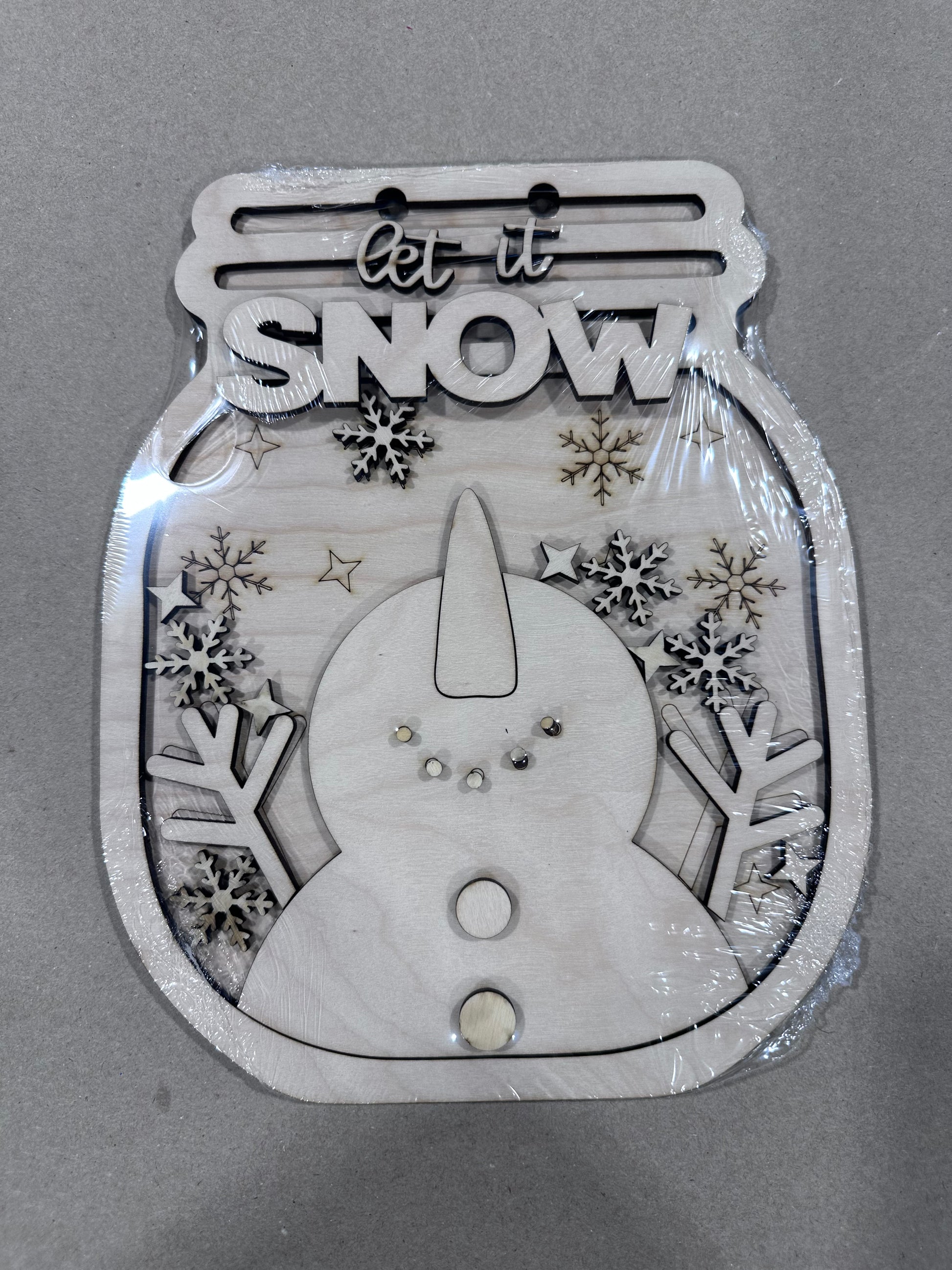 Wintery snowman in a mason jar-shaped wooden sign. Snowman is catching snowflakes, head tilted up.