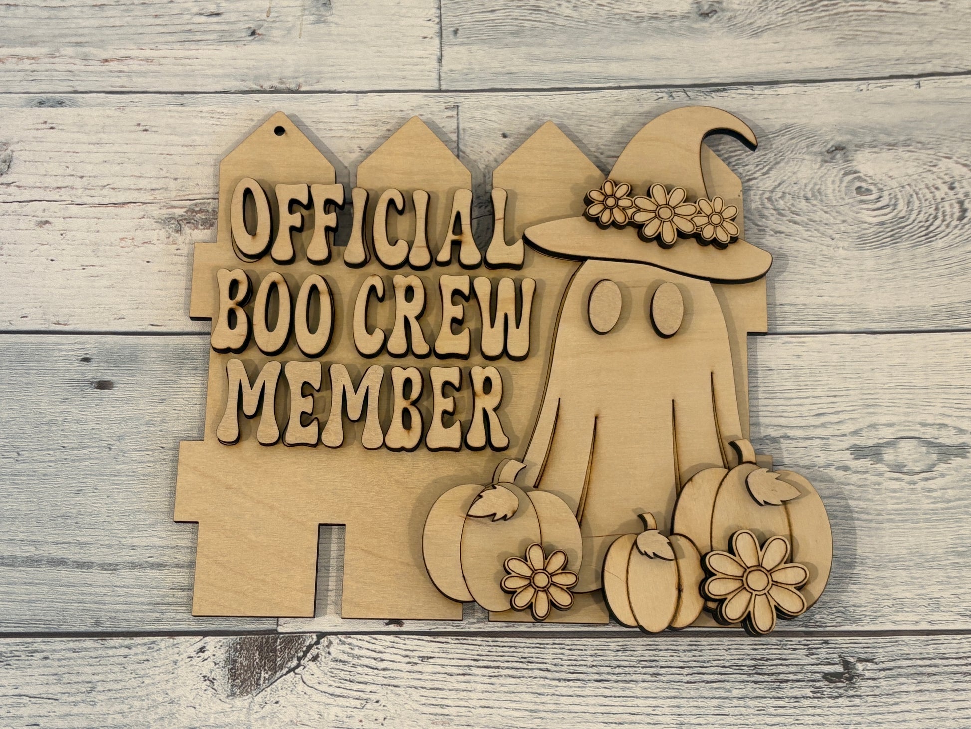 Laser cut sign of a fence with a ghost surrounded by pumpkins on it. Ghost has flowers on hat, farmhouse chic decor.