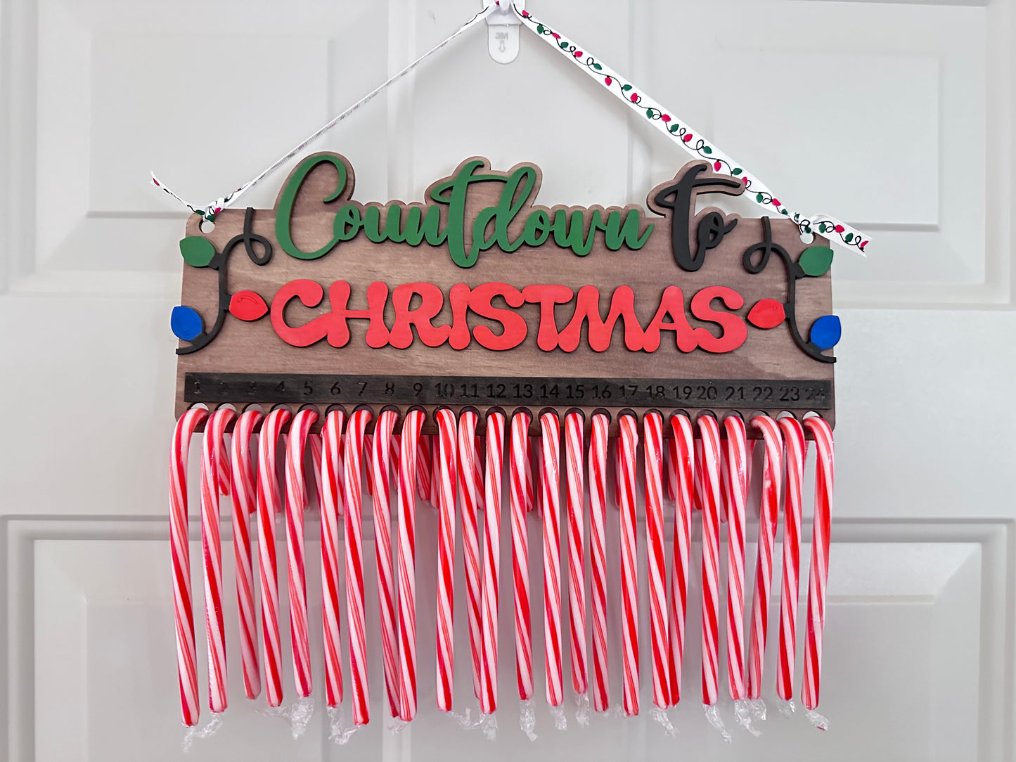 A wooden sign with 'Countdown for Christmas' text, decorated with candy cane stripes in red and white, and a green bow.