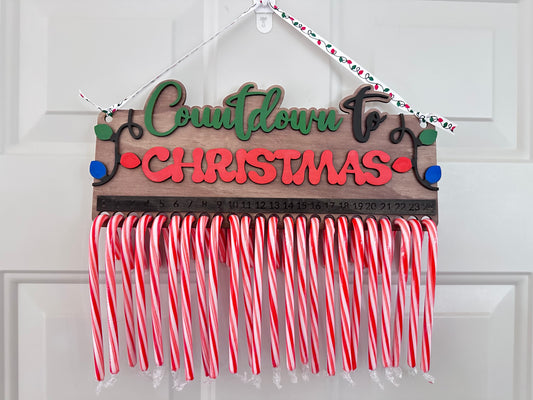 A wooden sign with 'Countdown for Christmas' text, decorated with candy cane stripes in red and white, and a green bow.