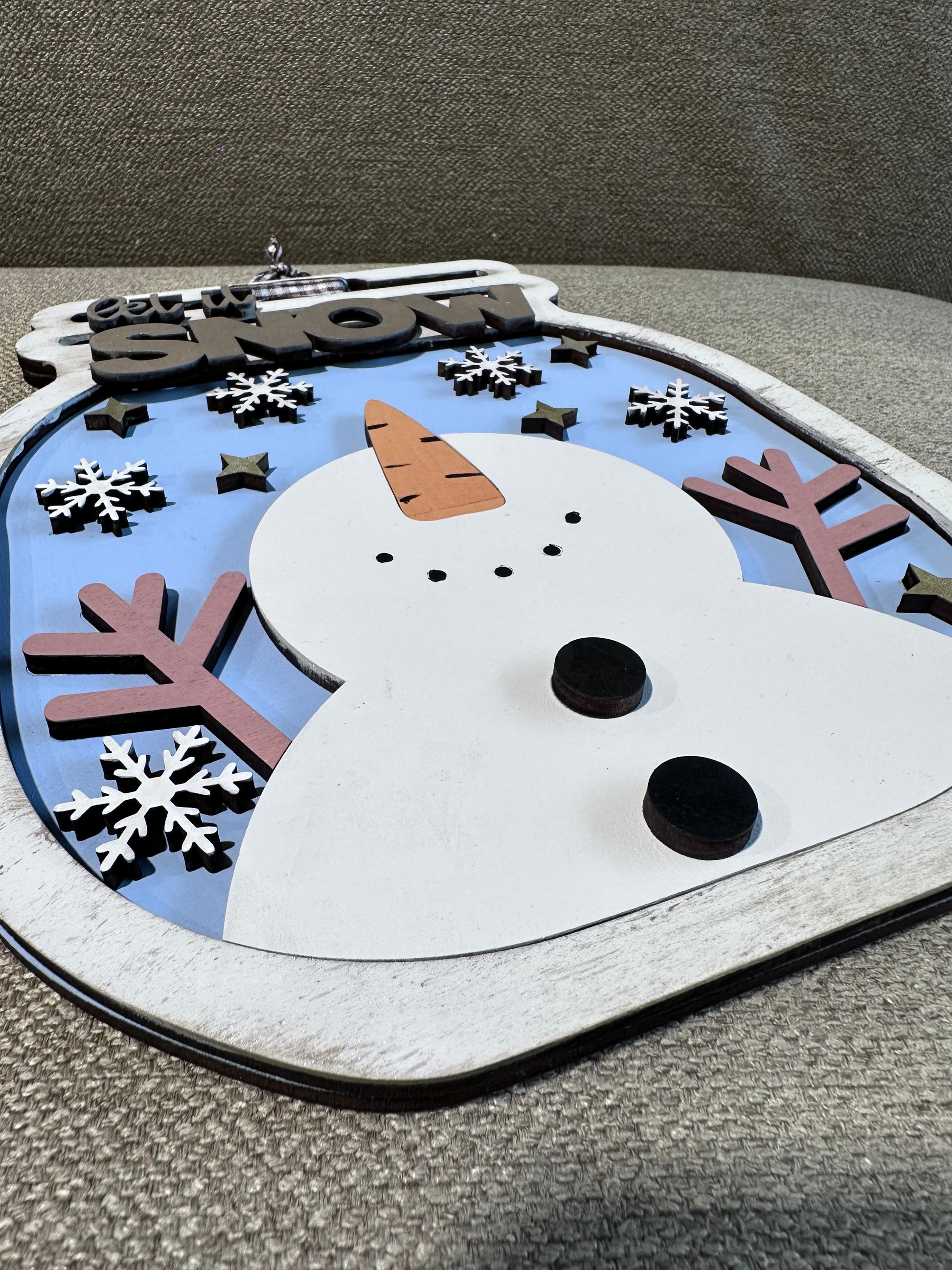 A close up of a snowman sign with silver dry brushing on a mason jar shaped wintery sign.