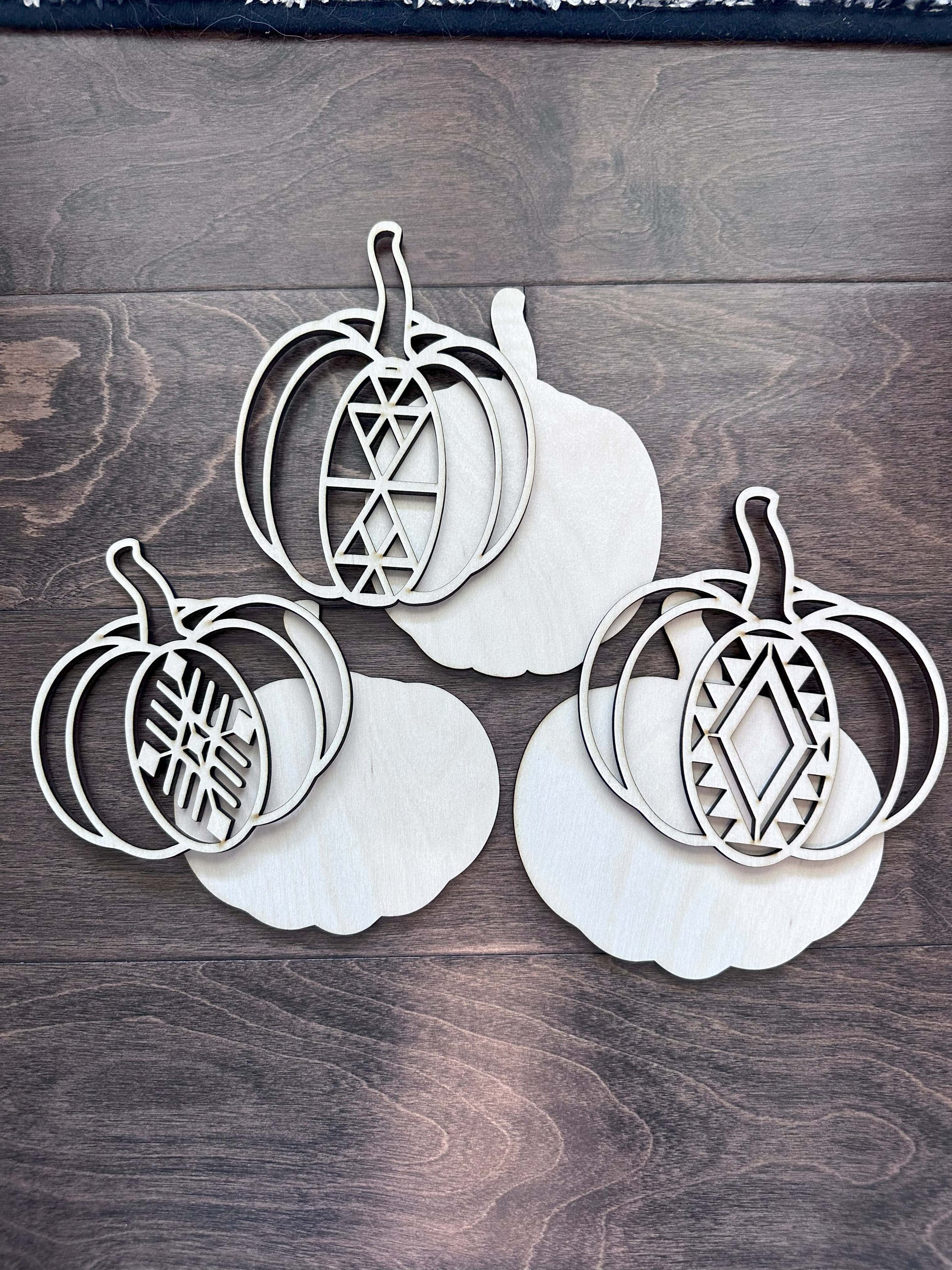 Three white pumpkin-shaped cutouts with geometric patterns, laser cut birch material.